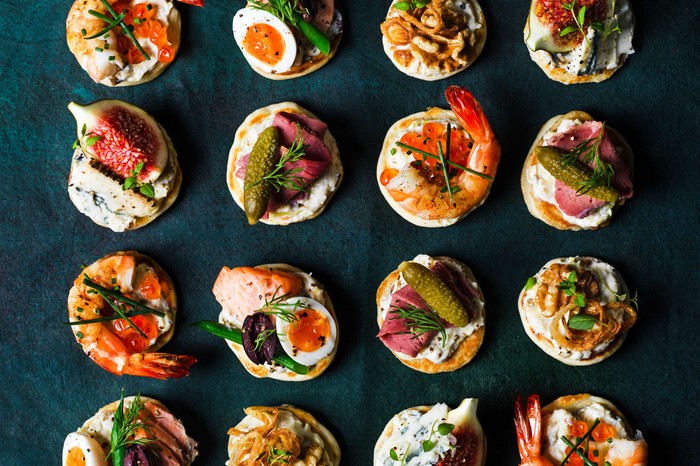 Dozens of blinis with different toppings on them on a serving platter