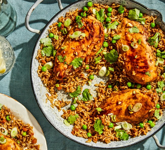 A Large Pan of Brown Rice Topped with Chicken Breasts and Spring Onions