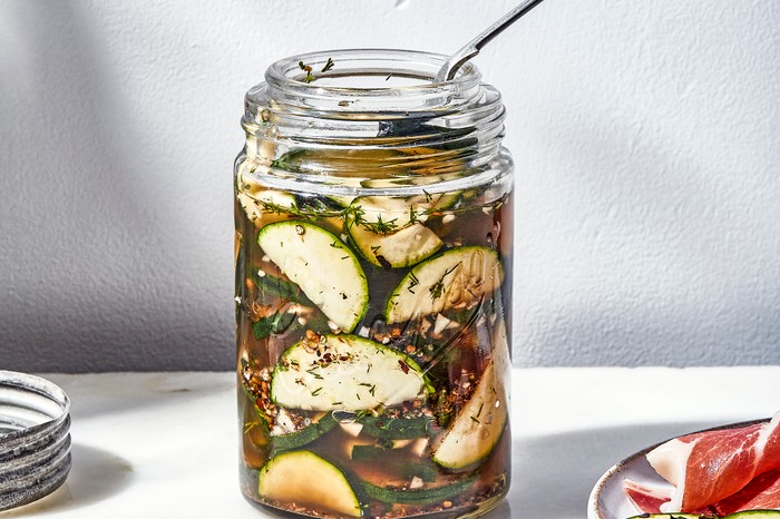 A glass jar of sliced courgettes in brine with a white background