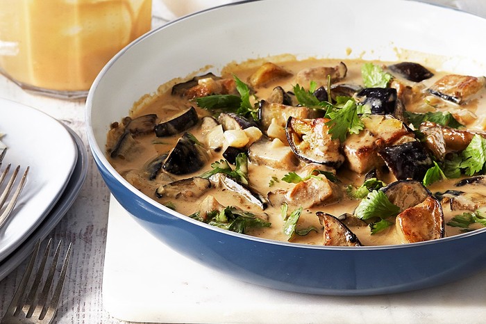 Coconut and Peanut Aubergine Curry Recipe | Eggplant Curry Recipe Bowl of creamy aubergine curry with a plate of forks and rice at the side