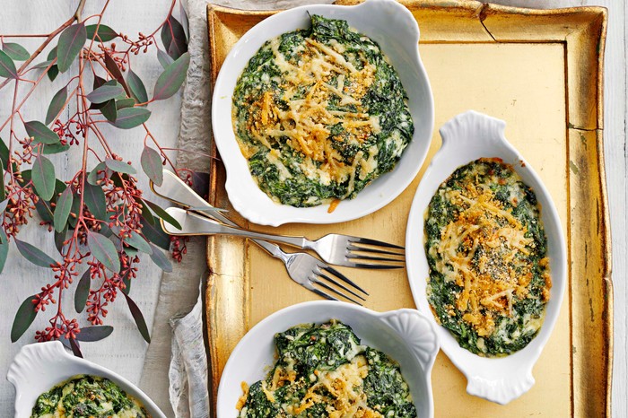 Three white bowls filled with a green spinach gratin with melted cheese on top