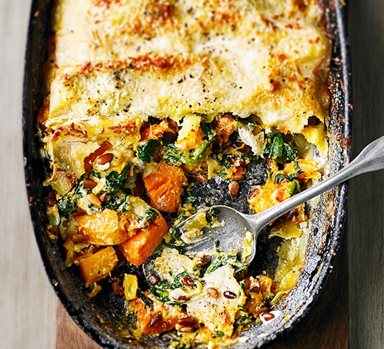 Butternut squash lasagne Butternut squash, spinach and mascarpone lasagne in a large oval black baking dish, placed on a wooden plank