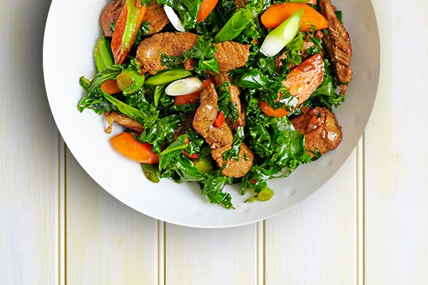 Pork Stir-Fry Recipe with Spring Onions and Kale served in a round white bowl on a light wooden table