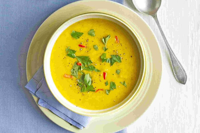 Two bowls of butternut squash soup, topped with chilli flakes and herbs