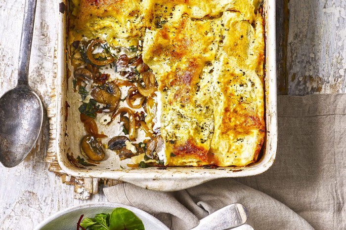 Caramelised onion, spinach and mushroom lasagne in a large rectangle baking dish with a large serving spoon next to it