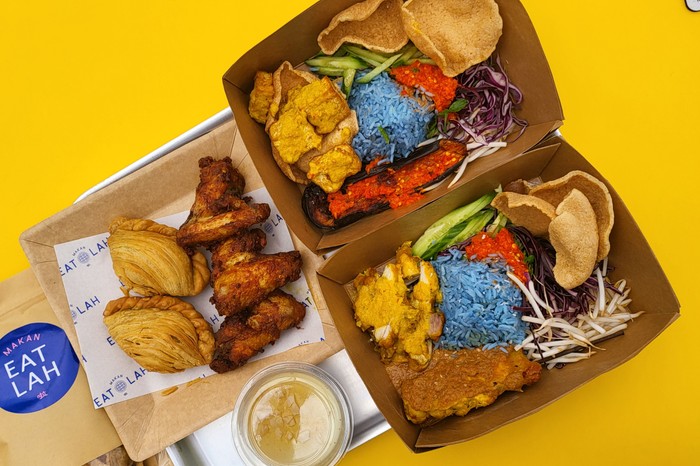 Two boxes of Nasi Kerabu, a blue-hued rice salad topped with plenty of veg and garnished with herbs, grated coconut, fish crackers and its own spicy sambal