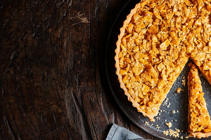 A wooden background topped with a golden pastry tart with cornflakes on top