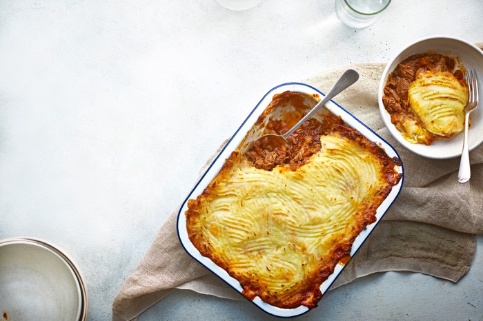 A white baking dish filled with a meat pie topped with mashed potato
