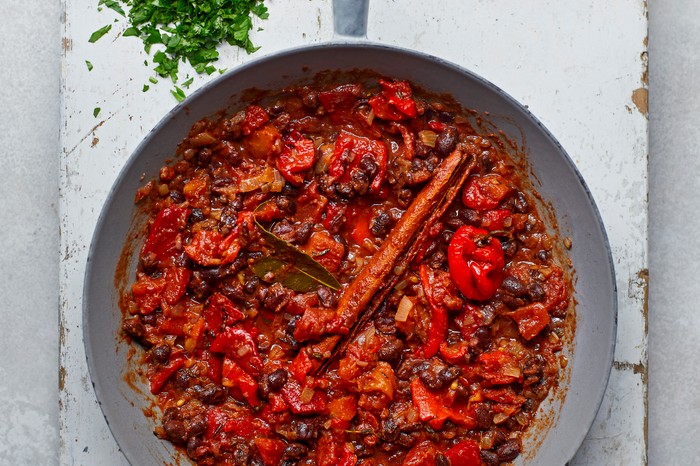 a silver pan with a wooden handle on a white wooden chopping board filled with pan of a bright-red coloured curry