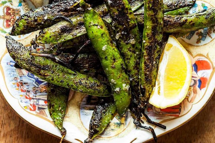 Grilled pea pods on plate with slice of lemon