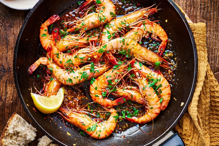 A pan containing 11 shell-on king prawns with a slice of lemon