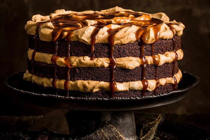 A multi layered chocolate cake with burnt butterscotch frosting, served on a black cake stand