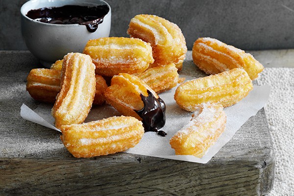 Churros Recipe with Hot Chocolate Dipping Sauce A handful of small churros next to a pot of hot chocolate dipping sauce