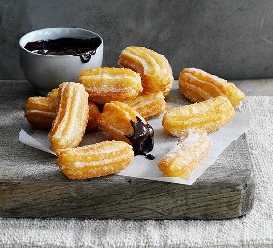 A handful of small churros next to a pot of hot chocolate dipping sauce