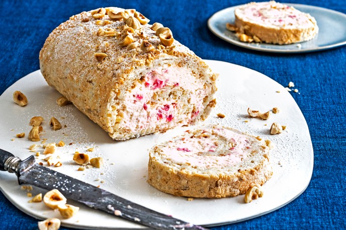 A roulade on a white plate with a blue fabric background with a slice cut off the end and a knife to one side