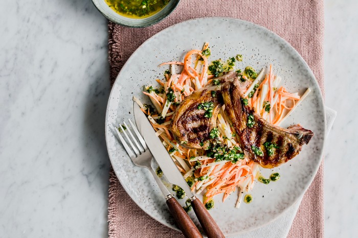 A plate topped with two grilled lamb chops and a shredded carrot and celeriac salad with green herbs