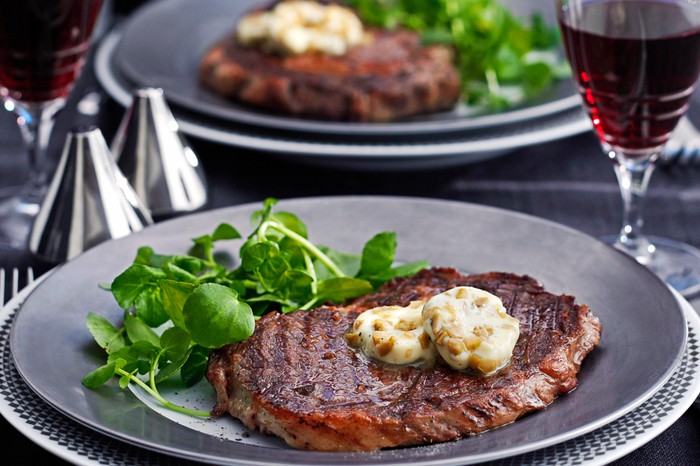 Rib-eye steak on a plate topped with dirty martini butter and served with lettuce