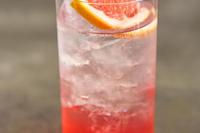 Highball glass filled with ice and grapefruit slice, orange coloured drink