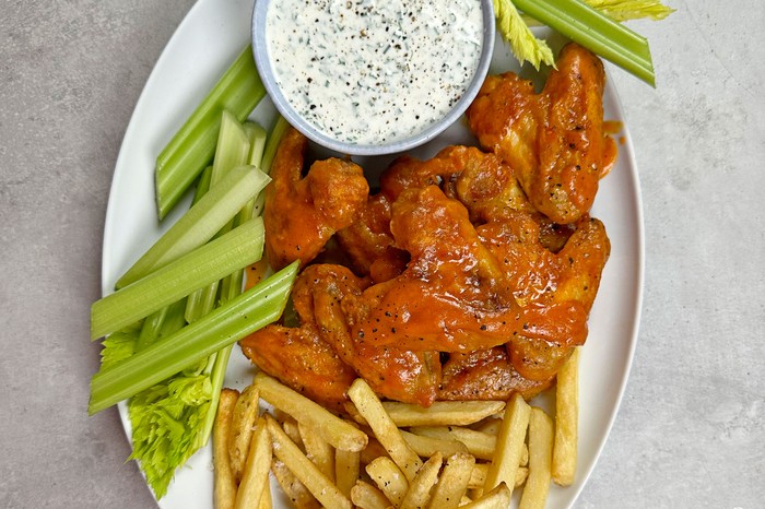 Platter of chicken wings, celery sticks and chips next to bowl of dip