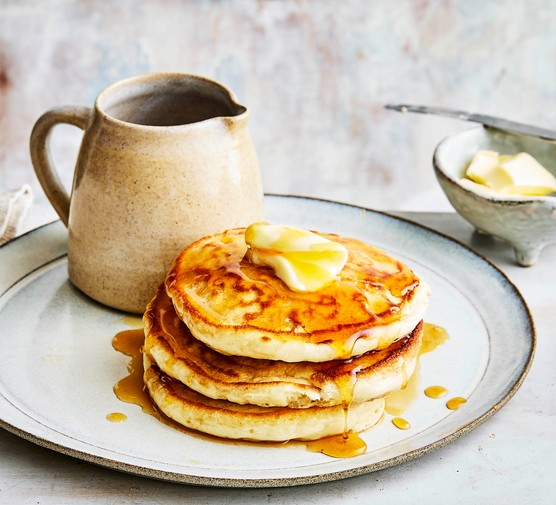 American pancakes in a stack next to a jug of maple syrup