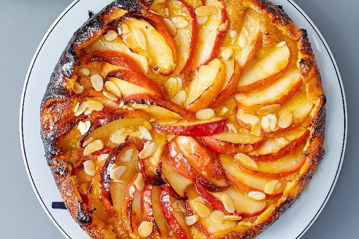 A round white plate toped with Apple and almond galette scattered with flaked almonds