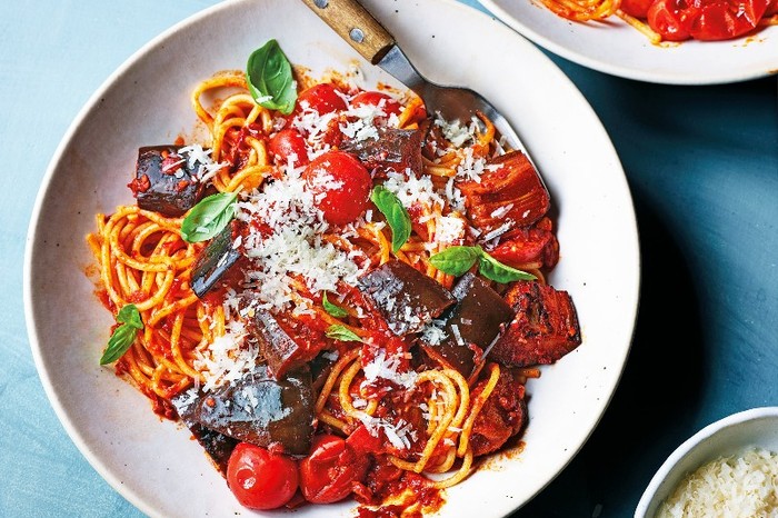 a bowl of spaghetti in a red sauce with chunks of aubergine and a wooden handled fork