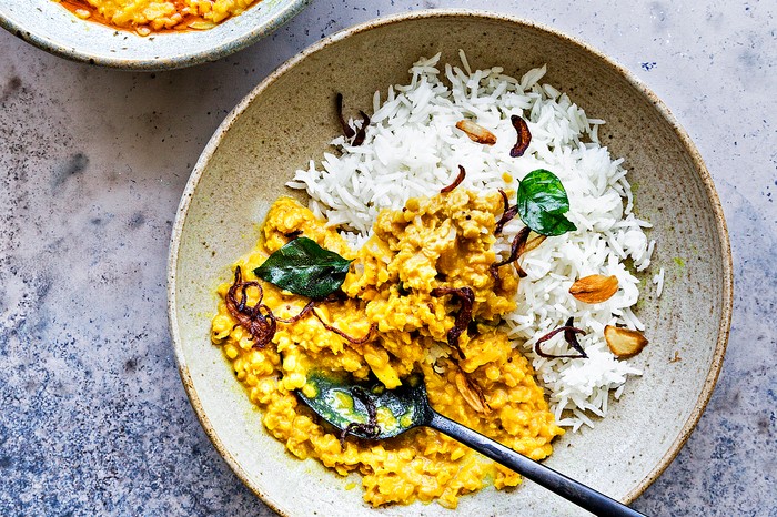 A white bowl filled with a golden-coloured curry and white fluffy rice, scattered with coriander on a grey stone background