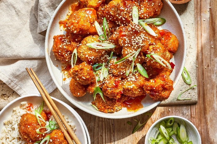 A serving bowl of bang bang cauliflower with a small potions on a plate over rice with chopsticks