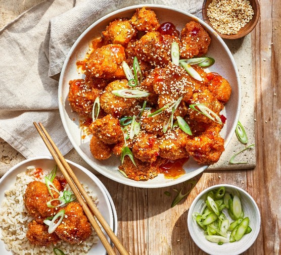 A serving bowl of bang bang cauliflower with a small potions on a plate over rice with chopsticks