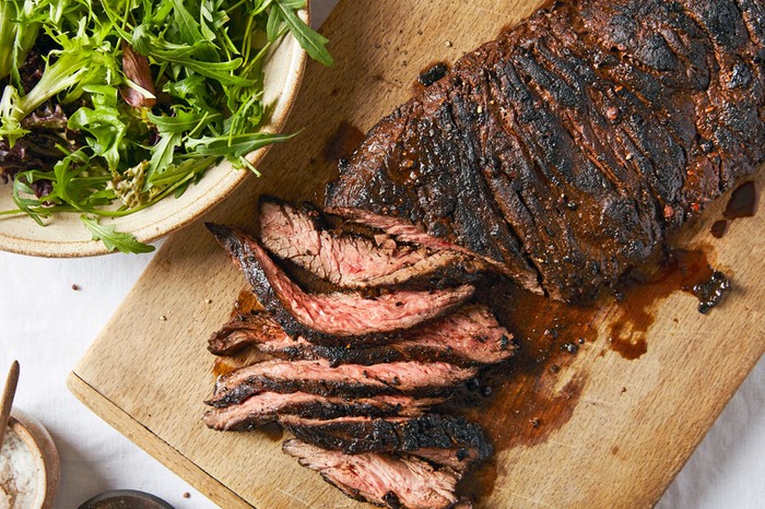 Sliced steak on a wooden chopping board next to a side salad