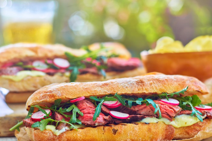 a sub-style sandwich packed with steak, rocket and radishes on a concrete surface outside