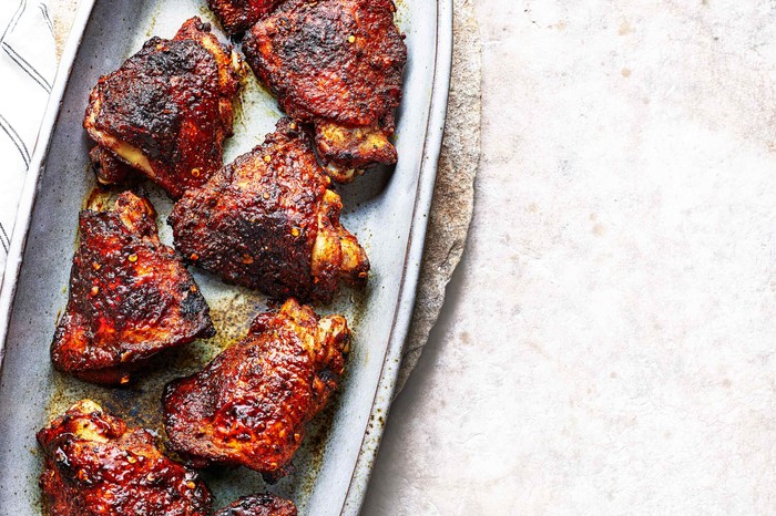 An oval platter topped with six BBQ chicken thighs with a red and blackened skin