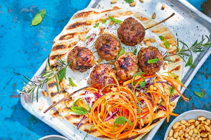 A silver tray topped with a large grilled flatbread meatballs and slaw on a blue background