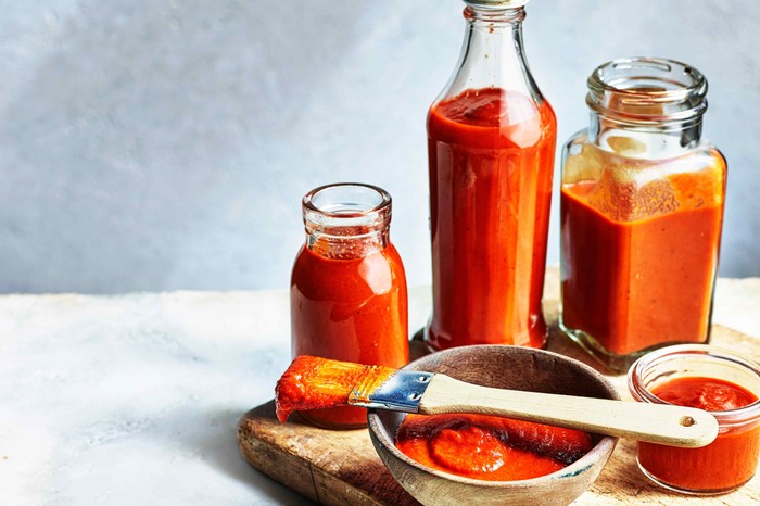 Three glass bottles and a small wooden dish all filled with a vibrant red sauce