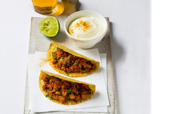 Bean chilli tacos, a pot of soured cream and lime wedge on a white slab