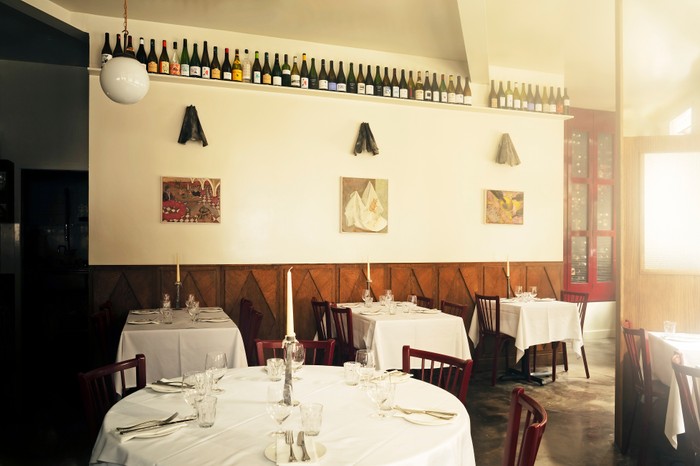 The interior at Bistro Freddie, including white tablecloths on tables, a bookshelf filled with wines running along the walls and wooden panelling