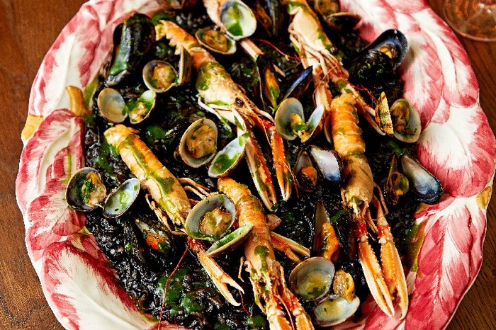 A red and white patterned bowl full of risotto with squid, clams and langoustines