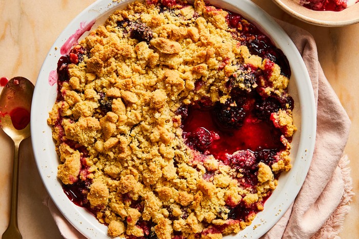 A dish of blackberry crumble with a portion taken out in a bowl at the side