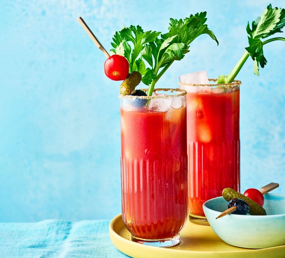 Two glasses of Bloody Mary cocktail with tomato and leaf garnish