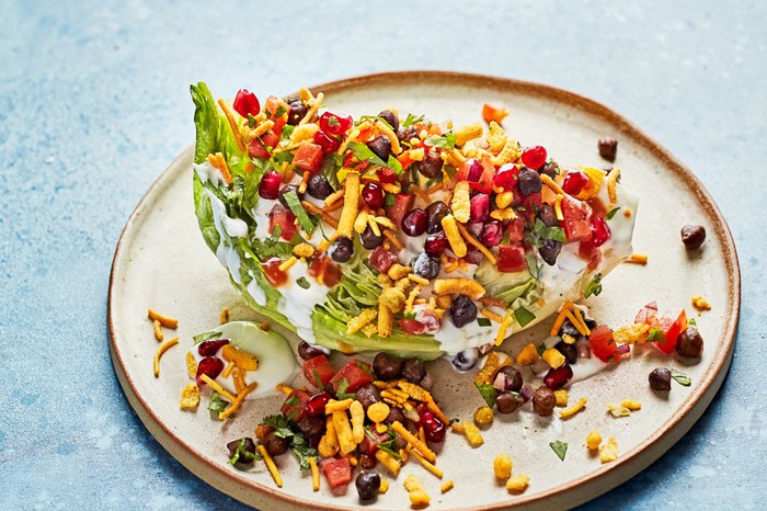 Lettuce topped with yogurt, bombay mix and pomegranate seeds on a plate