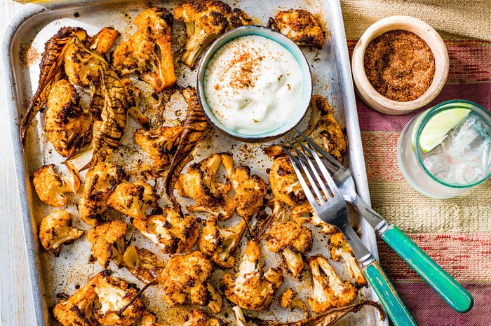 Roasted Cauliflower Florets with Tajín Recipe A silver tray topped with orange roasted cauliflower with a pot of white sauce in the corner