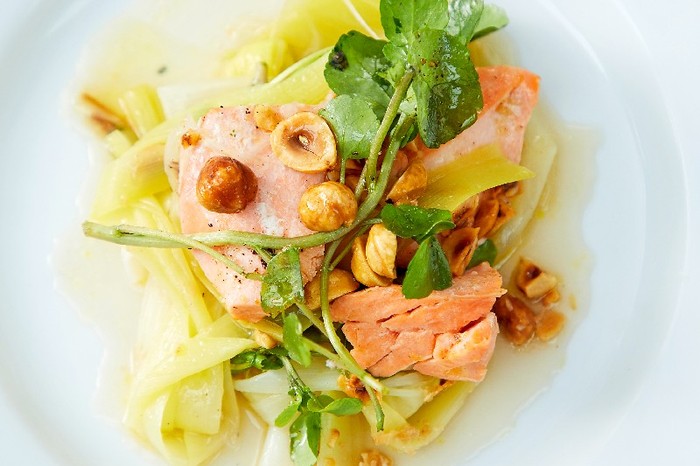 close up of Butter-poached trout, burnt leeks and hazelnuts on a white plate