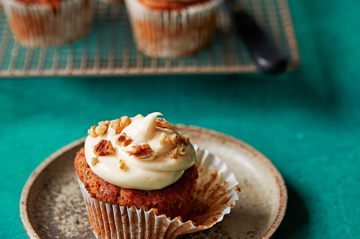 A teal background topped with a small plate, with a golden muffin with white icing on top