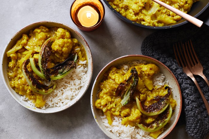 Two bowls of cauliflower curry with rice, placed next to each other with a set of cutlery to the right