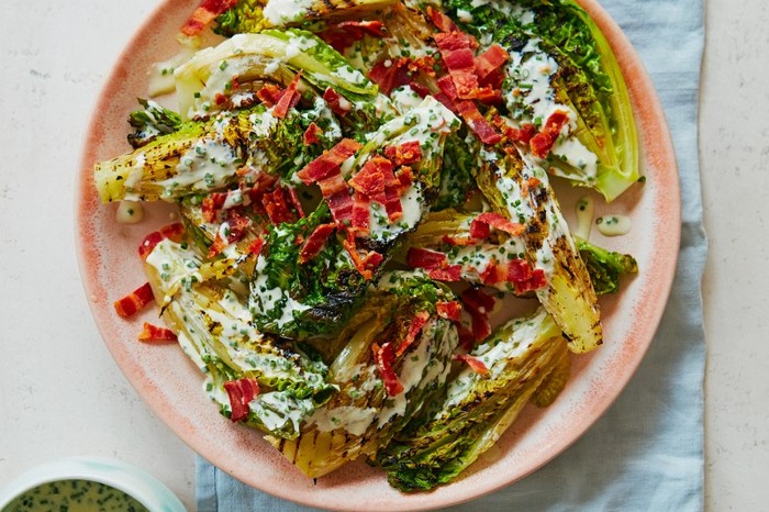 A plate of charred lettuce with creamy ranch dressing topped with bacon bits on a blue fabric napkin