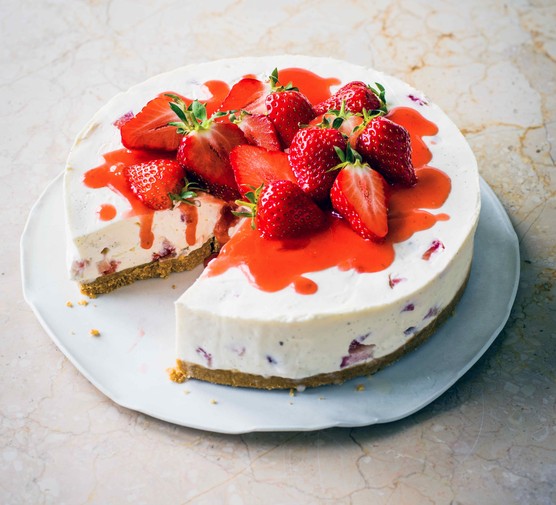 Strawberry Cheesecake Recipe A white cheesecake topped with red strawberries and whole strawberries on a white plate