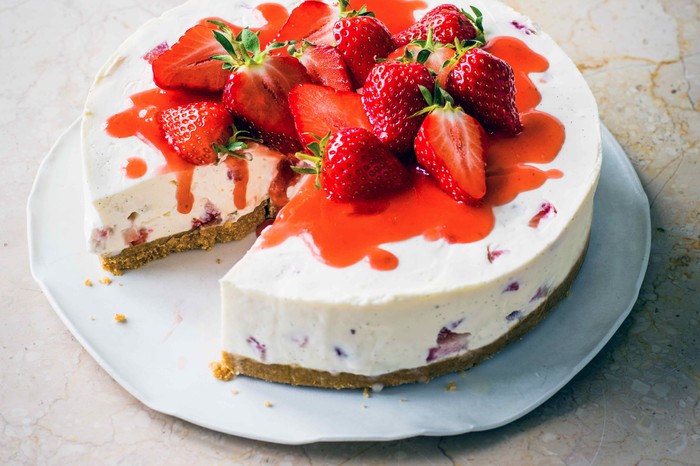 A white cheesecake topped with red strawberries and whole strawberries on a white plate