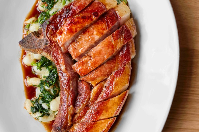 Tamworth Chop with Stewed White Beans at Orasay, Notting Hill A white oval shaped plate is topped with stewed white beans with bitter greens and slices of Tamworth pork chop