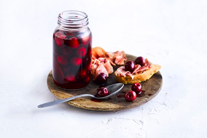 Pickled Cherries in a kilner jar served on a wooden board with ham and bread