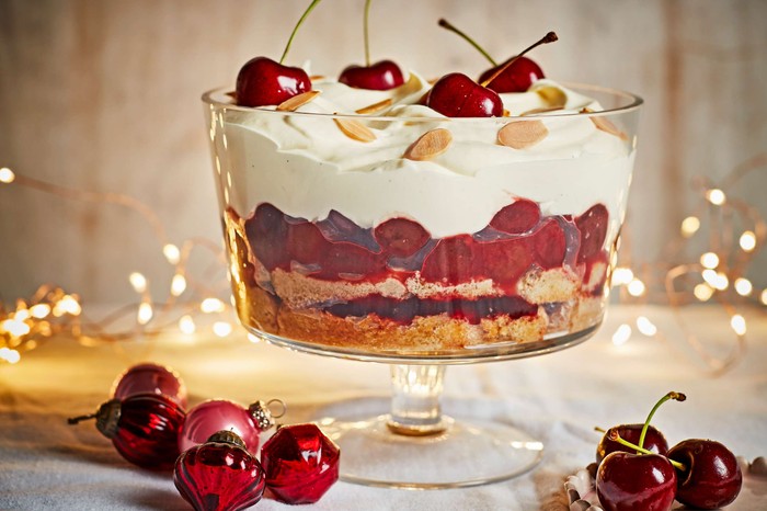 A cherry trifle in a large glass trifle bowl with fairy lights in the background